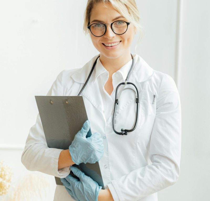 Portrait of a smiling female doctor in a lab coat with stethoscope and clipboard indoors.